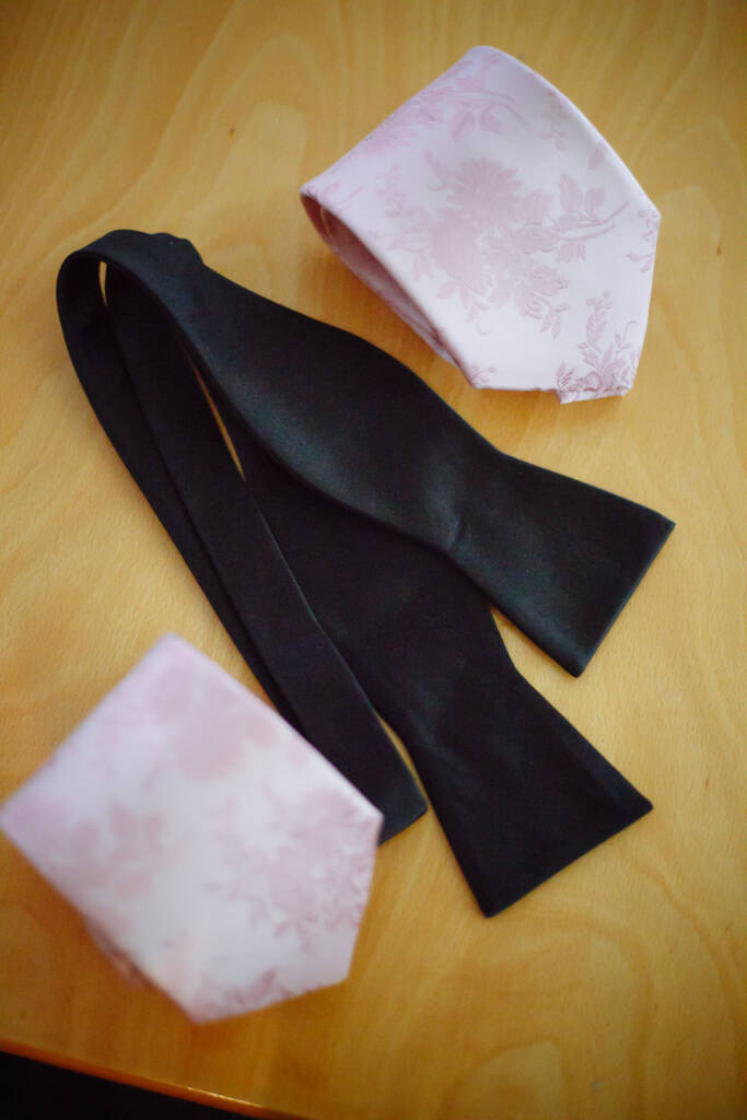 A self-tie black bow tie sprawls beside two blush floral ties
