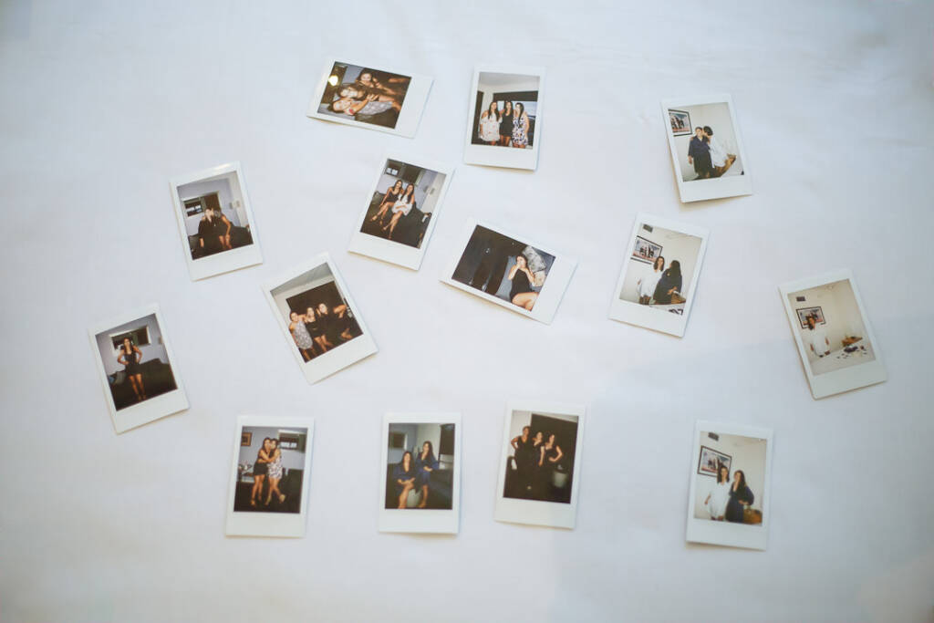 A scatter of instant snapshots of women in party dresses laid out on a white sheet.