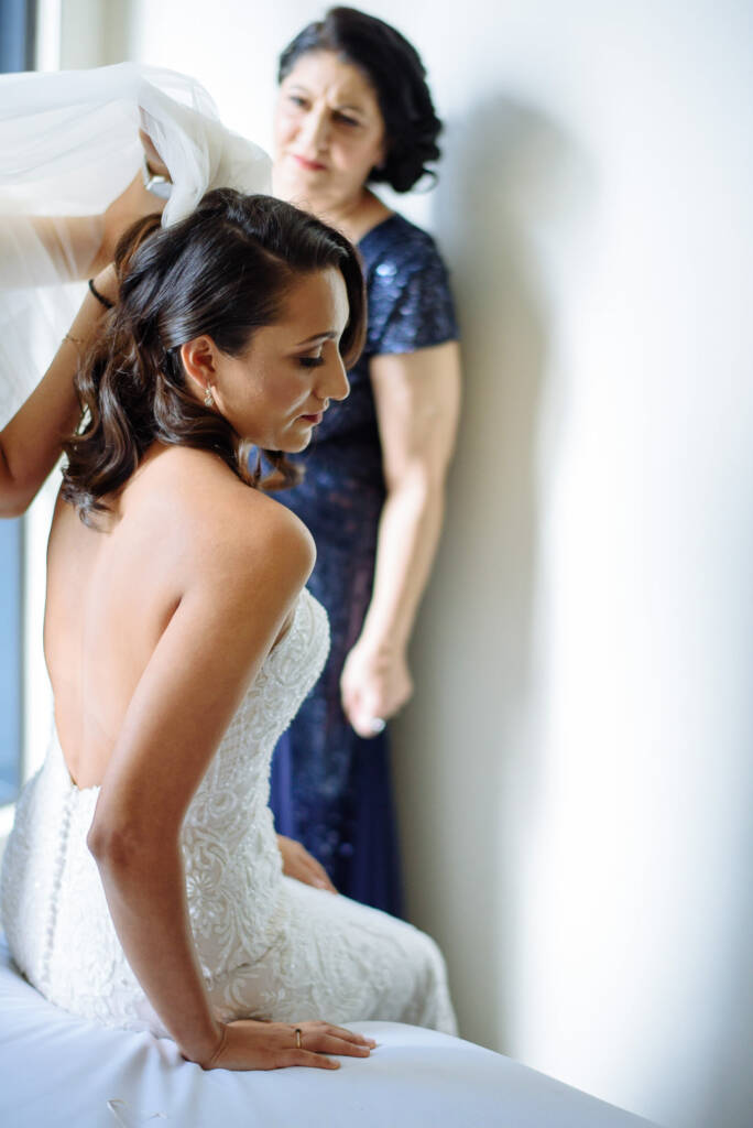 The woman in sequinned navy keeps watch as the veil comes over the bride's low bare back.