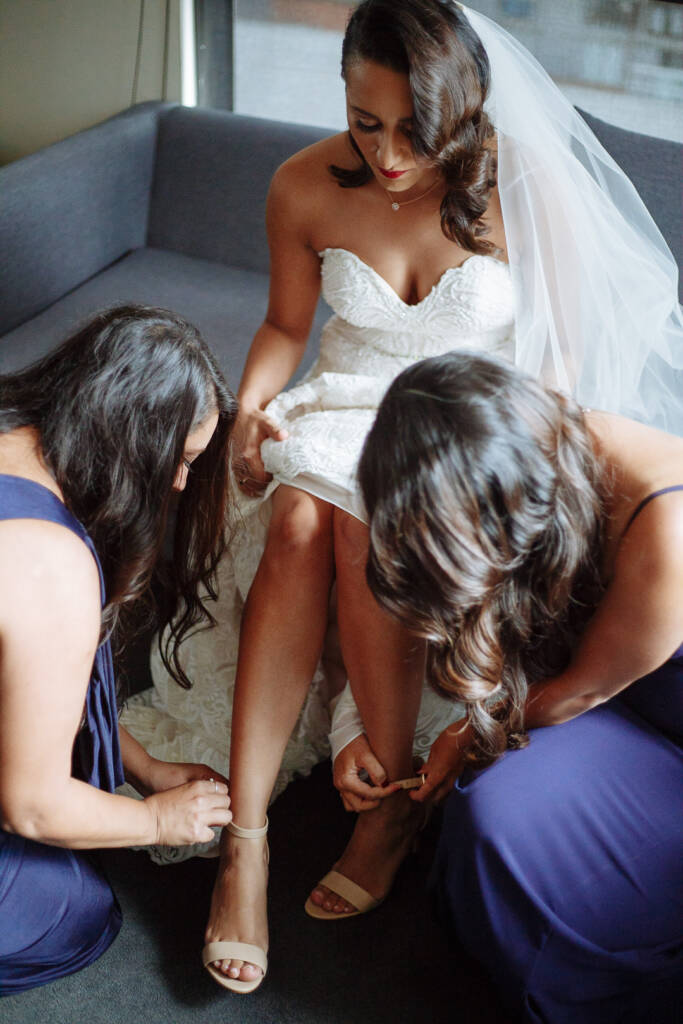 Both bridesmaids kneel to buckle the nude ankle straps