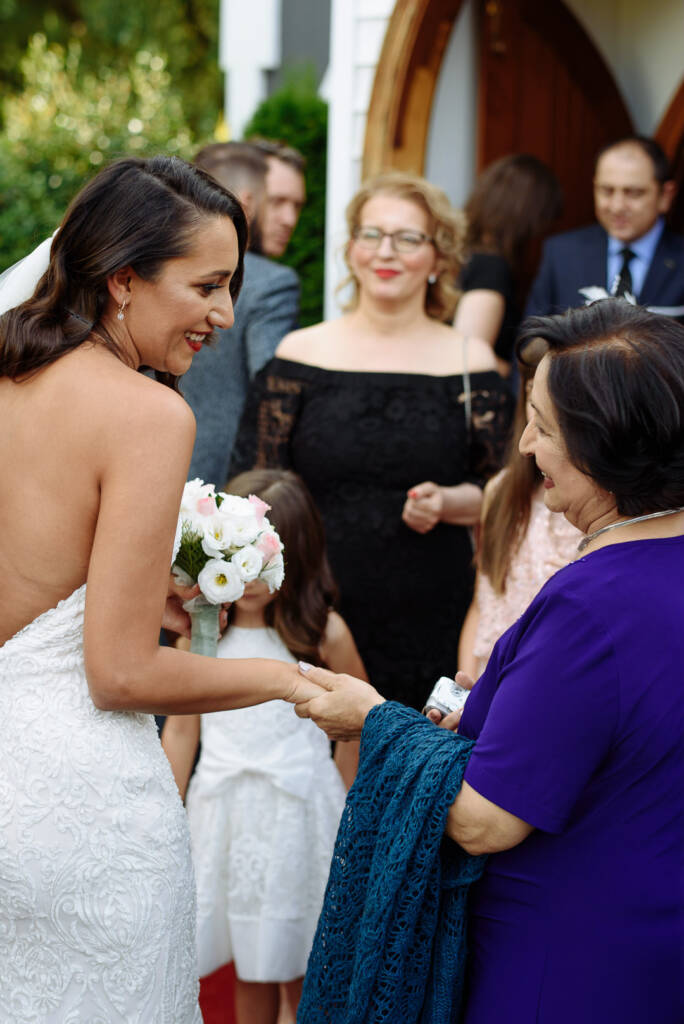 The bride laughs taking the hand of a woman in purple with a teal shawl, flower girls beside.