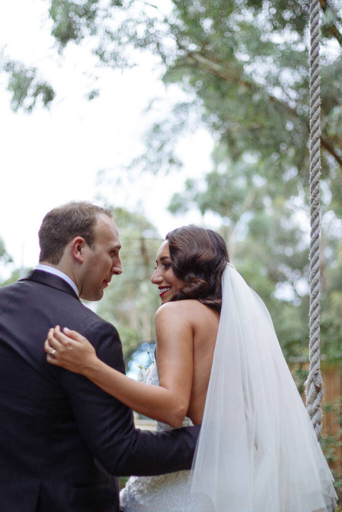 The bride glances back mid turn beneath the gums, veil streaming, the swing rope beside her.