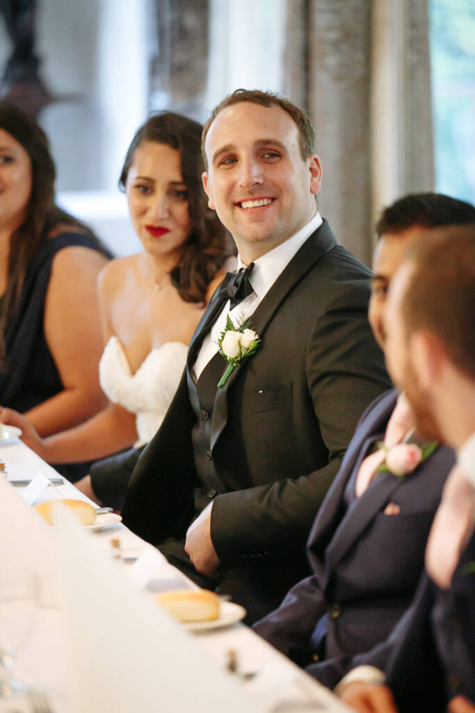 The groom glows down the table as the tributes land
