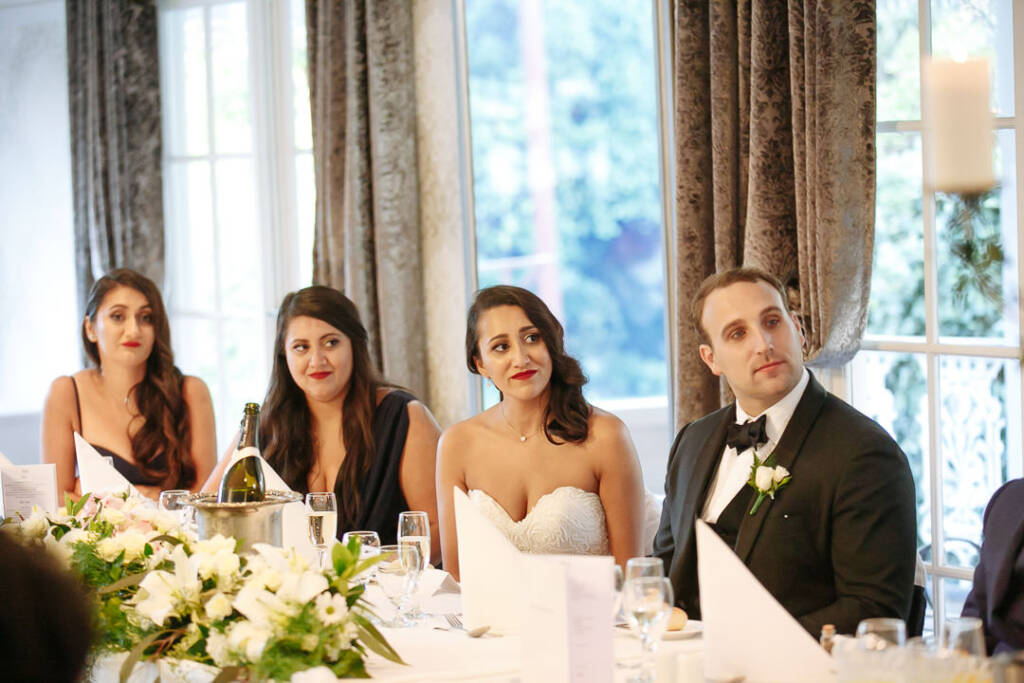 Bridesmaids and groom listen in, faces caught mid-story