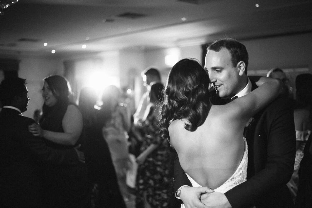Bare backed and beaming, the bride folds into the groom as the dance floor fills.