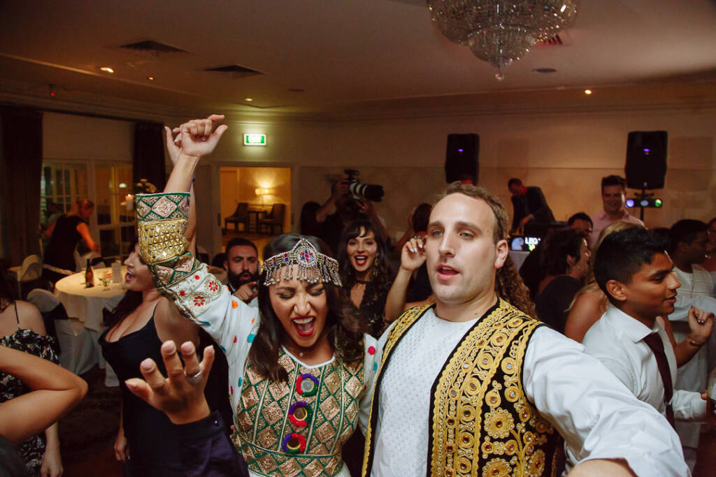 Headdress flashing, the bride and groom lead the late night dance circle in embroidered dress and vest.