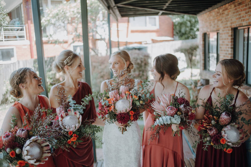Emma poses with four wedding attendants and their protea bouquets on the covered deck of a private home in Allambie Heights.