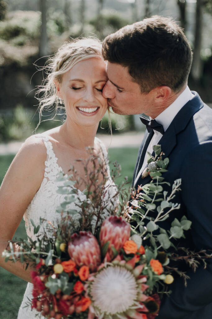 Sean kisses Emma’s cheek as she closes her eyes above her bouquet.
