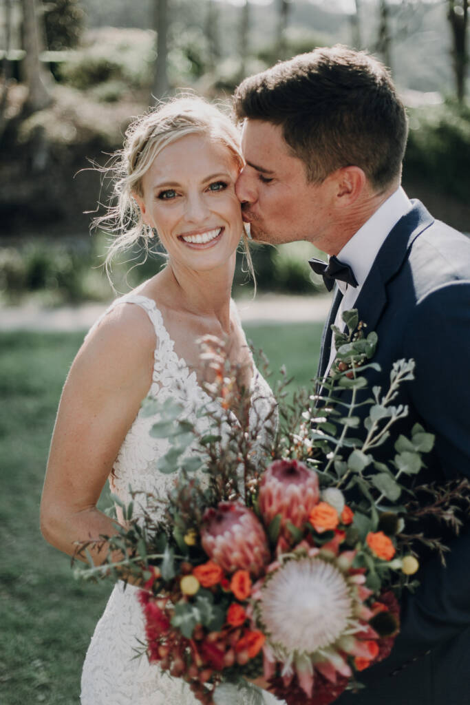 Emma smiles towards the camera as Sean kisses her cheek.