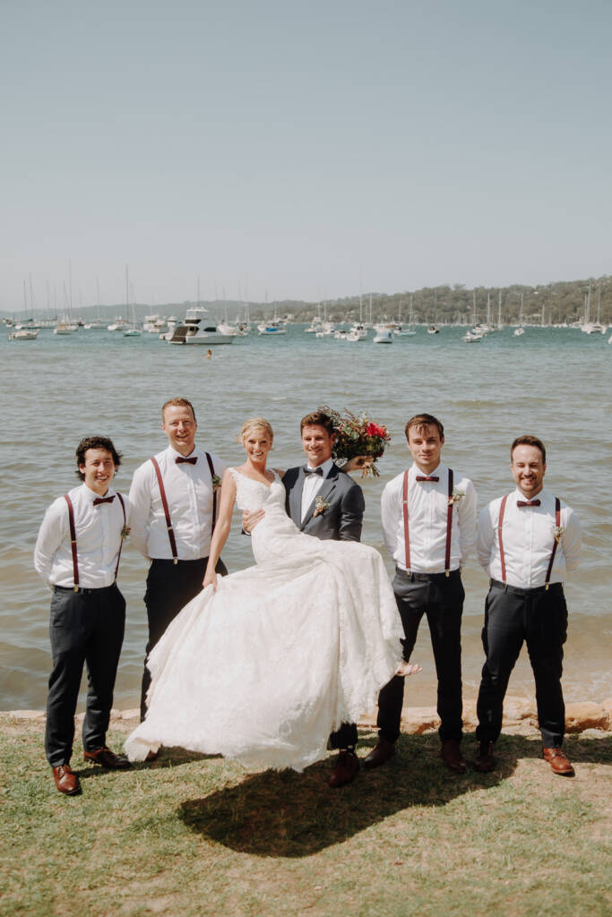 Sean carries Emma beside four wedding attendants on the lawn near Bayview Yacht Club.