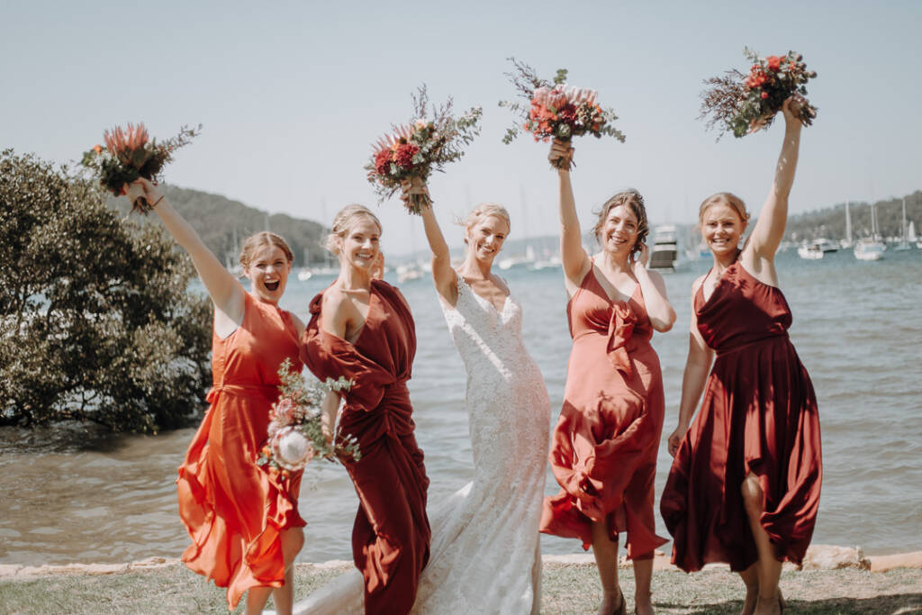 Emma and four attendants raise their bouquets beside the water near Bayview Yacht Racing Association.