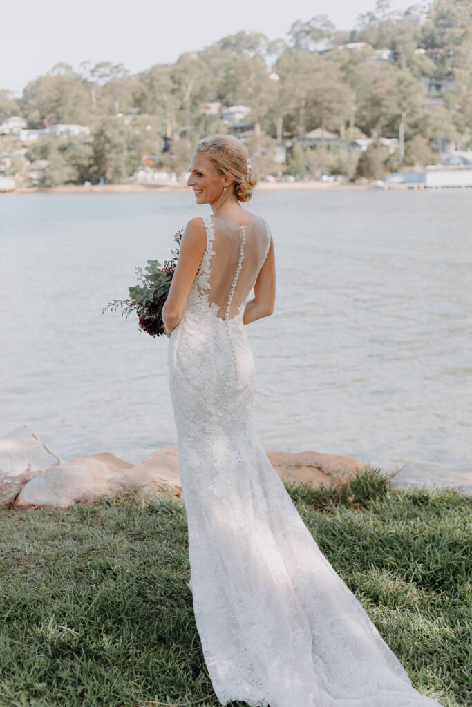 Emma’s buttoned lace gown is seen from behind beside Pittwater near BYRA.