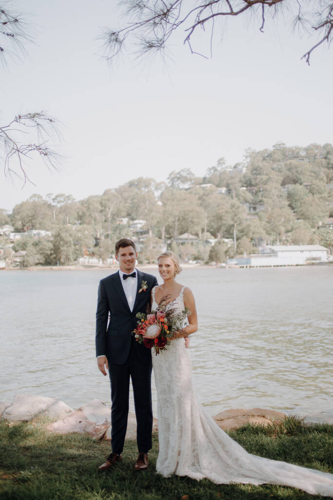 Emma and Sean pose by the water with Bayview Yacht Racing Association visible across the inlet.