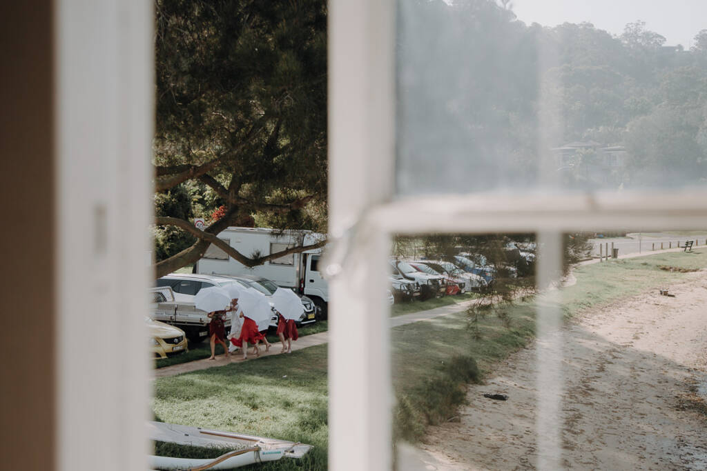 Wedding attendants carrying white umbrellas are seen through a Bayview Yacht Racing Association window.