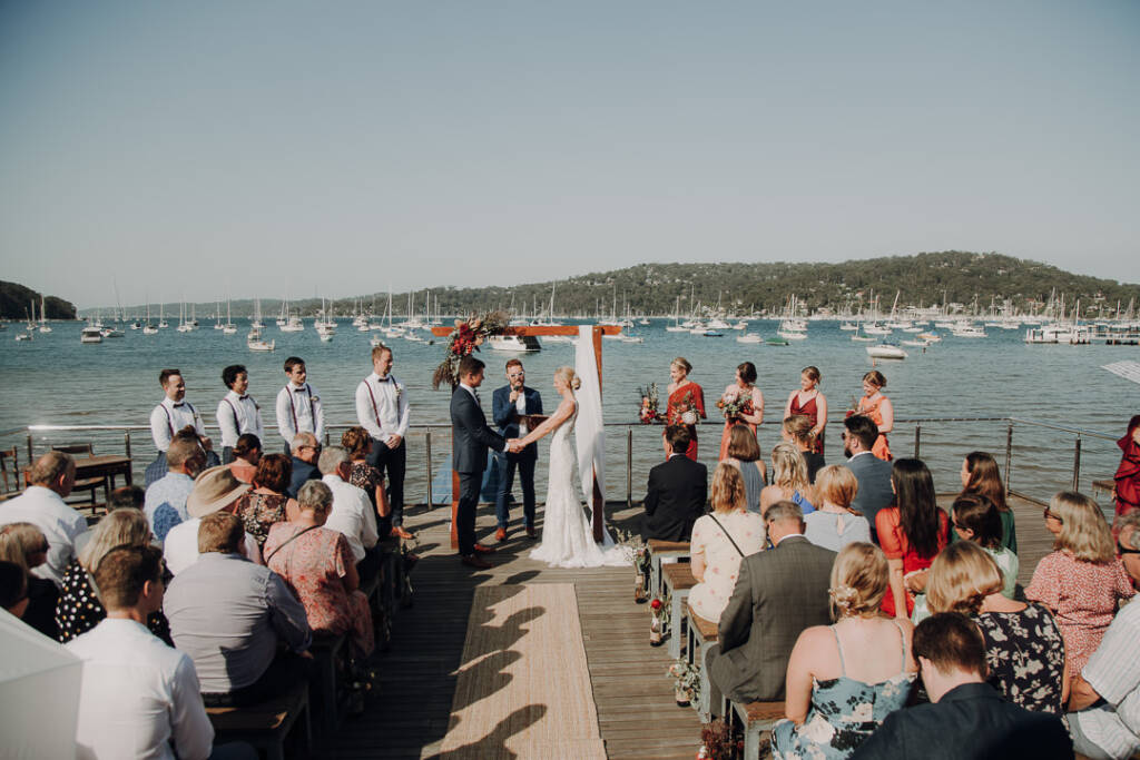 Emma and Sean stand beneath the arbour for their waterside wedding at Bayview Yacht Racing Association.