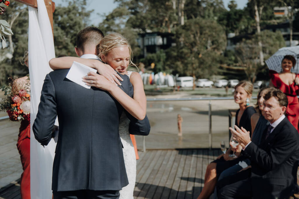 Emma hugs Sean with a sheet of paper in her hand as guests applaud.
