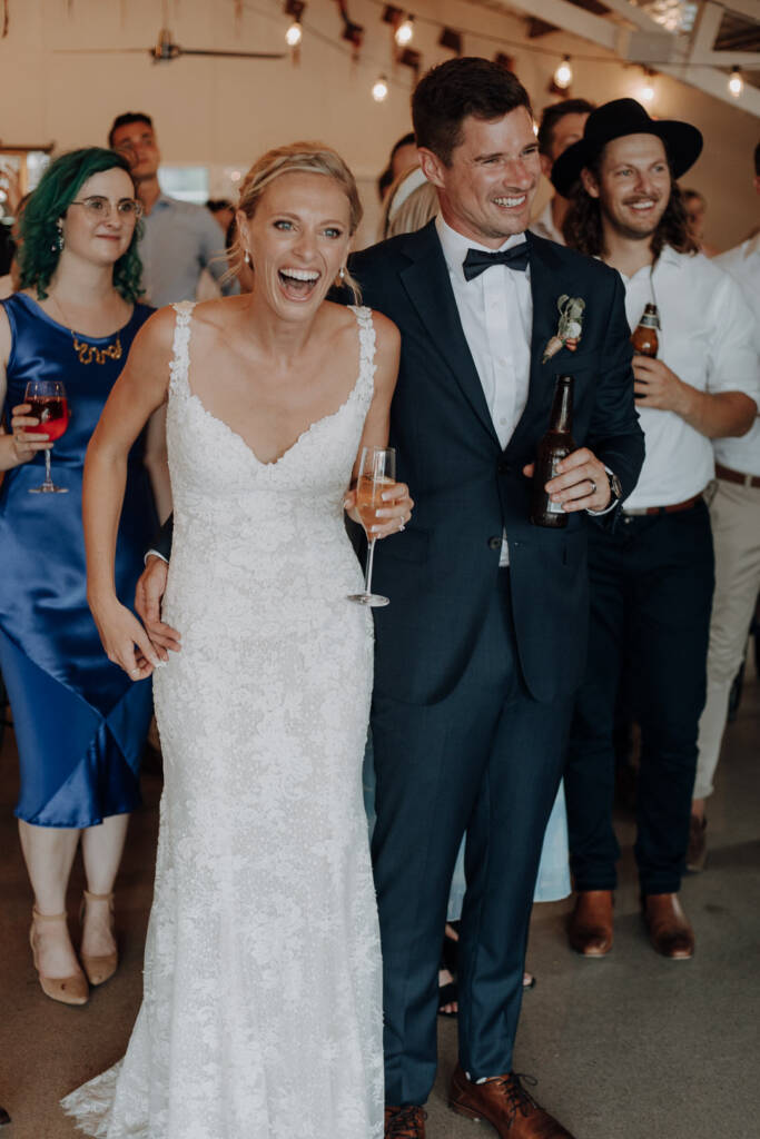 Emma and Sean laugh while holding hands and drinks during the wedding reception.