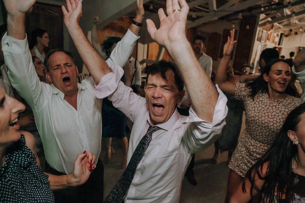 Wedding guests raise both arms while dancing at the reception.
