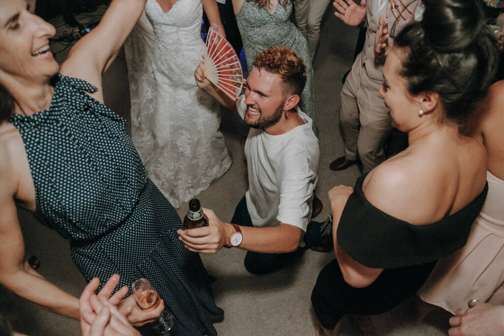 A guest kneels on the dance floor with a beer bottle and red folding fan.