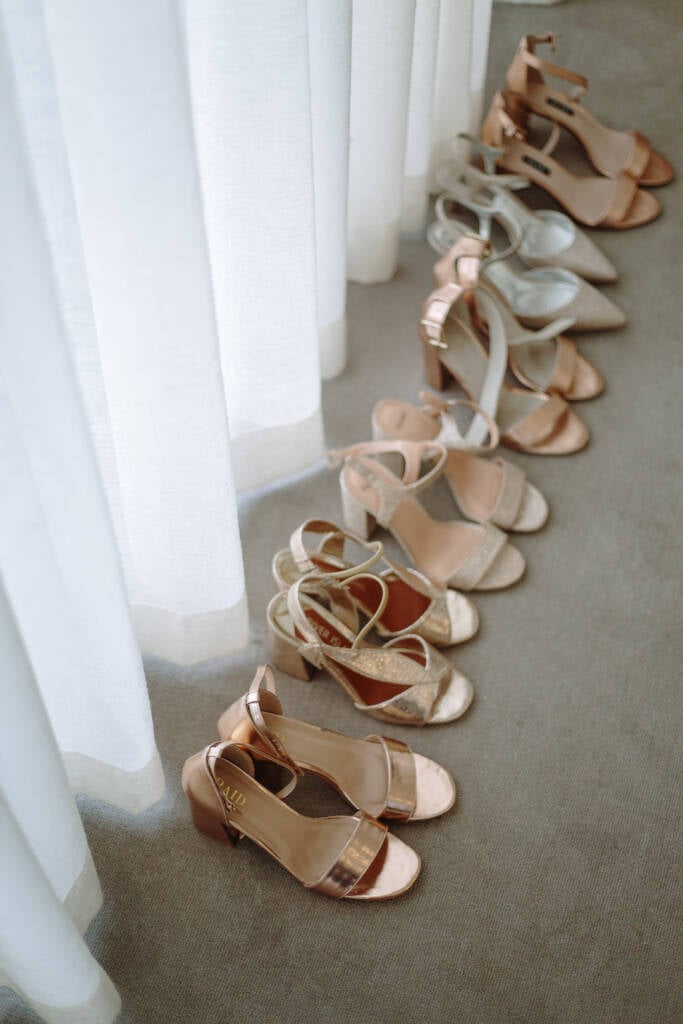 Rose-gold and silver bridal party shoes line the floor beside sheer curtains.