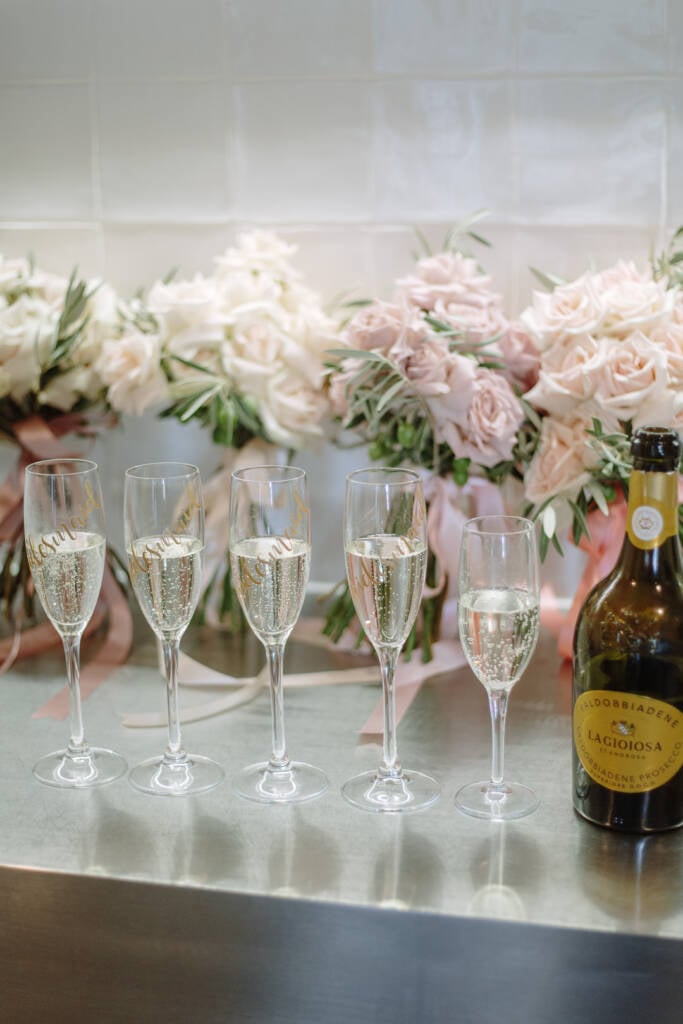 Personalised champagne flutes stand beside blush and white wedding flowers.