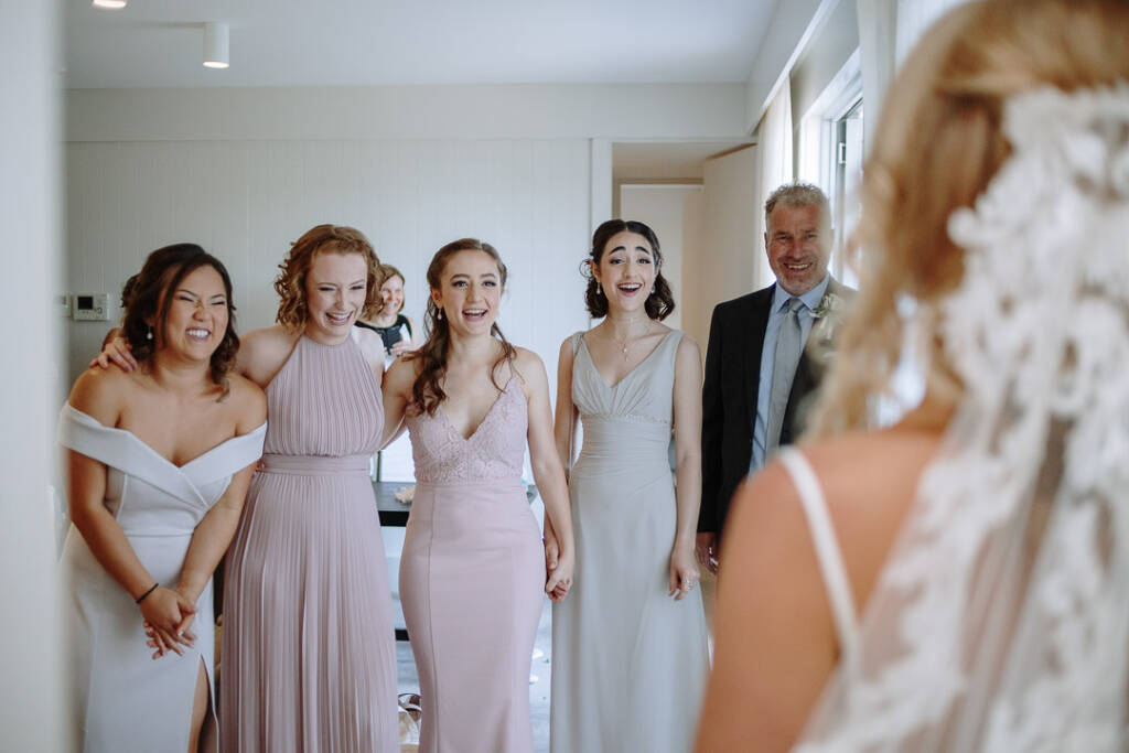 Becky's bridal party react with smiles and laughter when they see her in her wedding gown.
