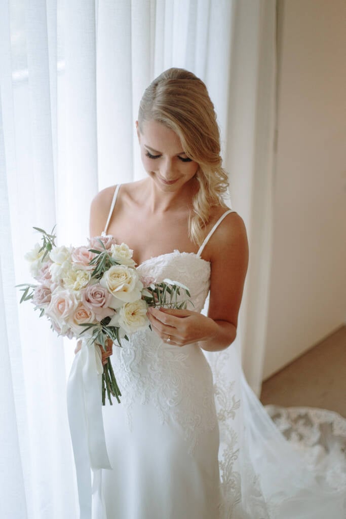 Becky smiles down at her pastel bridal bouquet with long trailing ribbons.