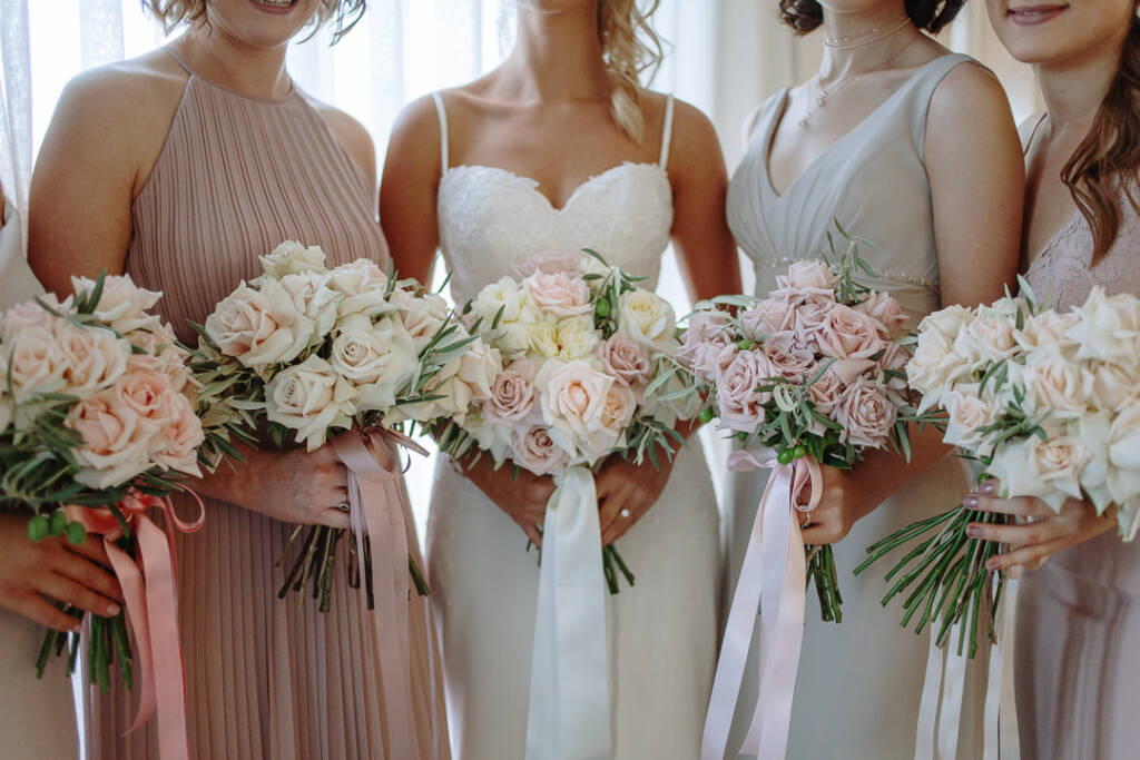 Becky and her bridesmaids hold blush and cream rose bouquets with trailing ribbons.