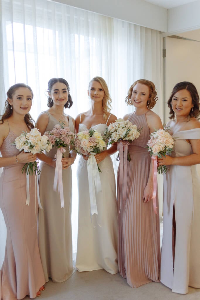 Becky poses with four bridesmaids in mismatched pastel dresses for a bridal party portrait.