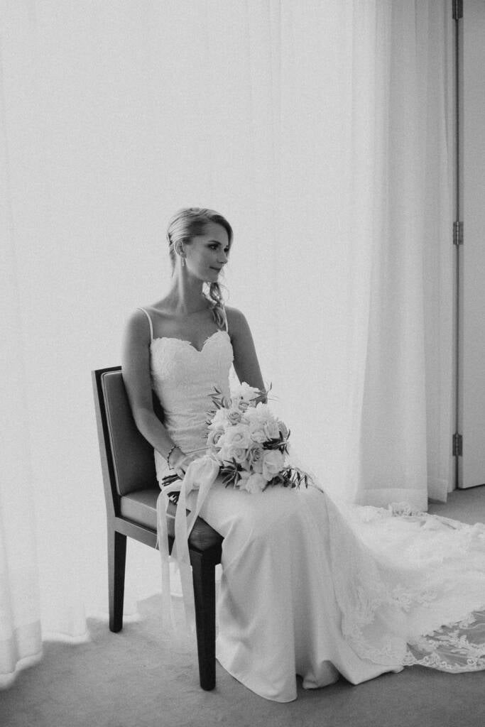 Black and white seated bridal portrait of Becky with her wedding bouquet resting on her knee.