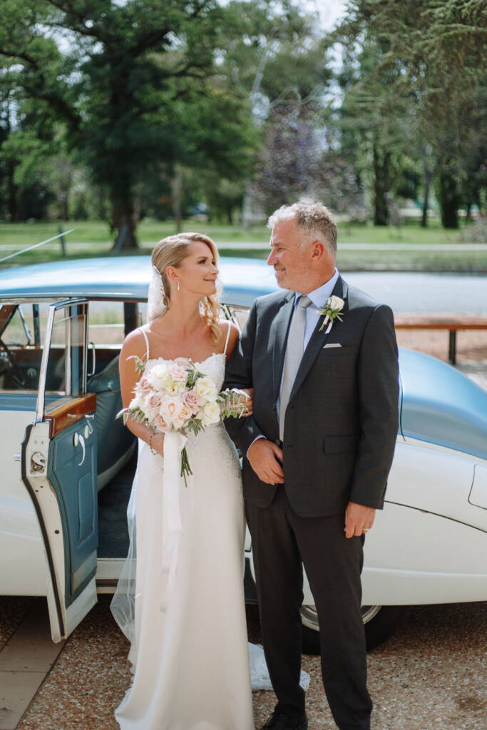 Becky stands with a loved one beside the vintage car outside St Nicholas Canberra.