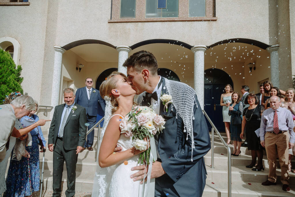 Becky and George kiss beneath falling petals outside St Nicholas Greek Orthodox Church, Canberra.