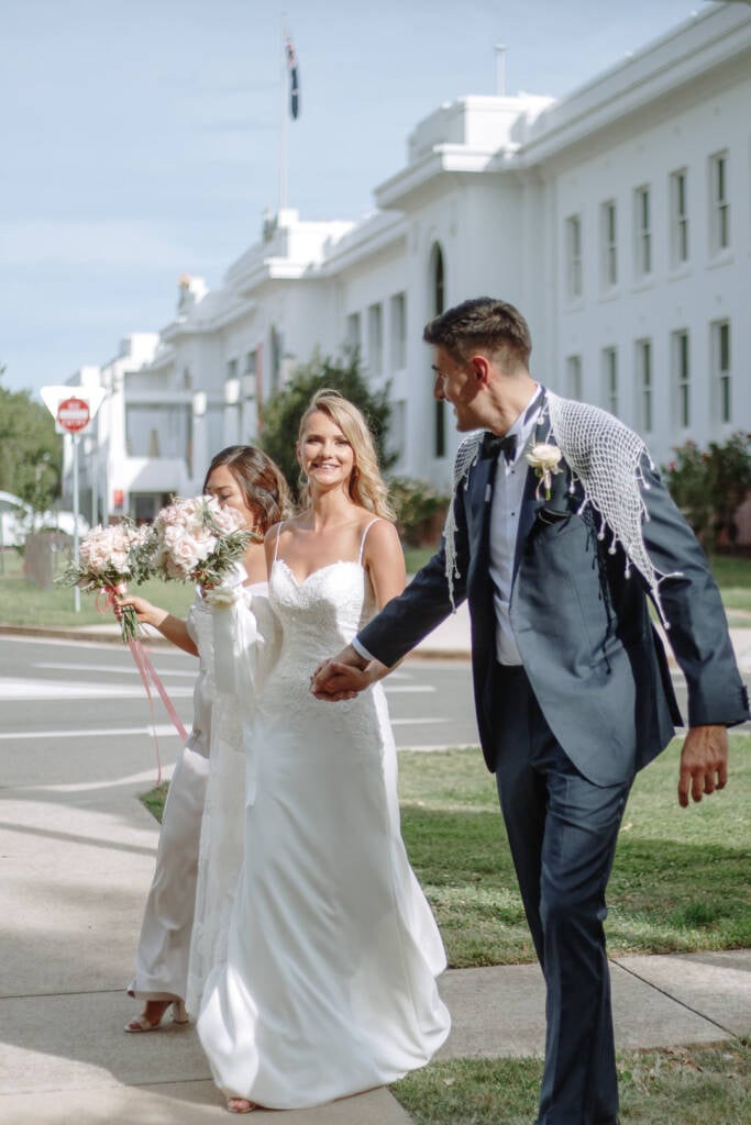 Becky and George walk beside the white facade during heritage garden portraits at Old Parliament House Gardens.