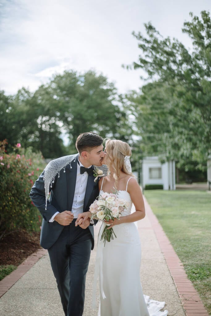Becky and George kiss while walking through Old Parliament House Rose Gardens Canberra.