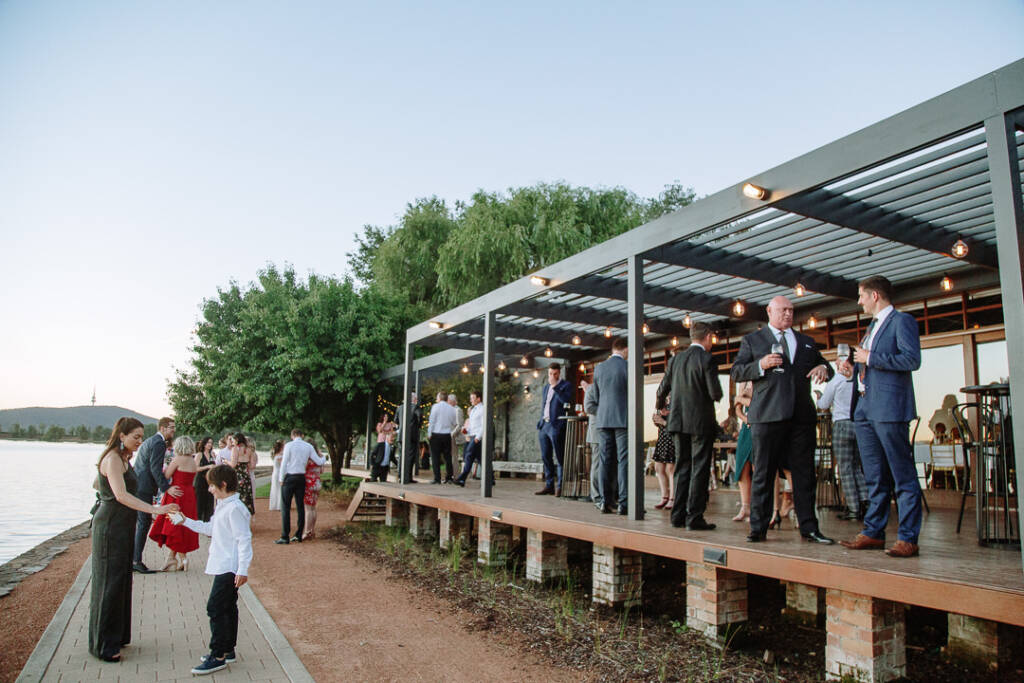 Guests gather on the waterfront deck at The Boat House in Canberra in golden evening light.