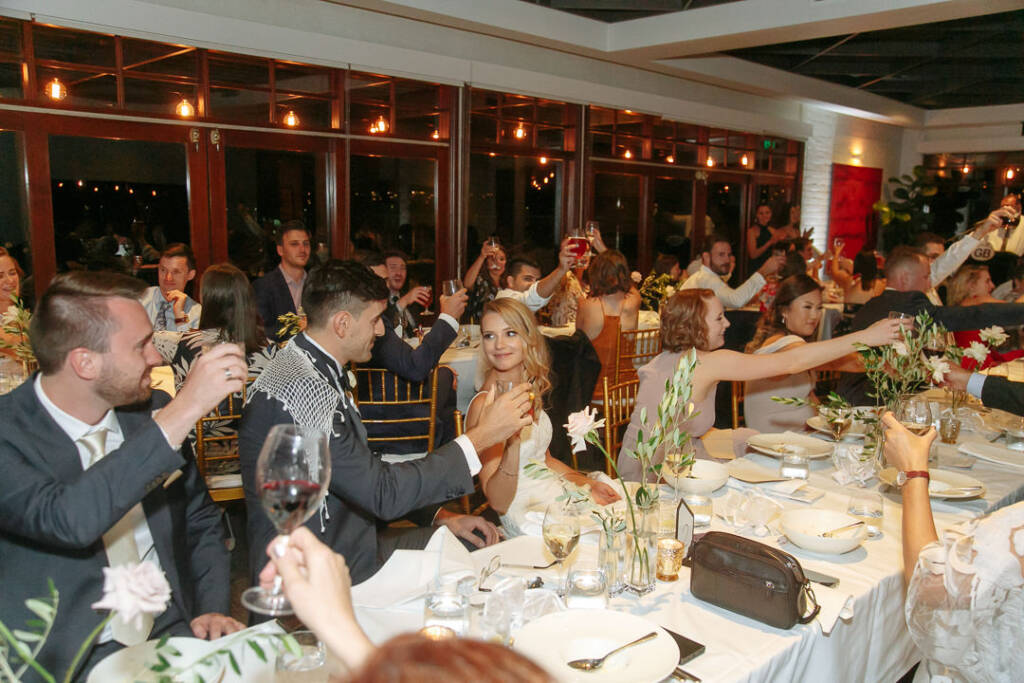 Wedding guests raise wine glasses during a reception toast.