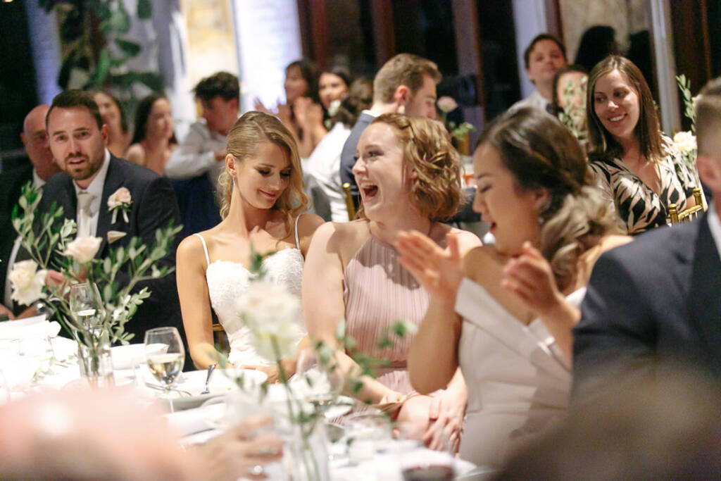 Bridesmaids laugh and applaud together during the reception speeches.