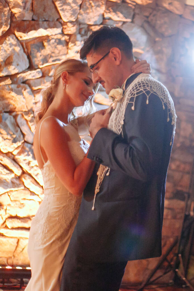 Becky and George share their first dance beside the amber-lit stone wall at Boat House by the Lake.