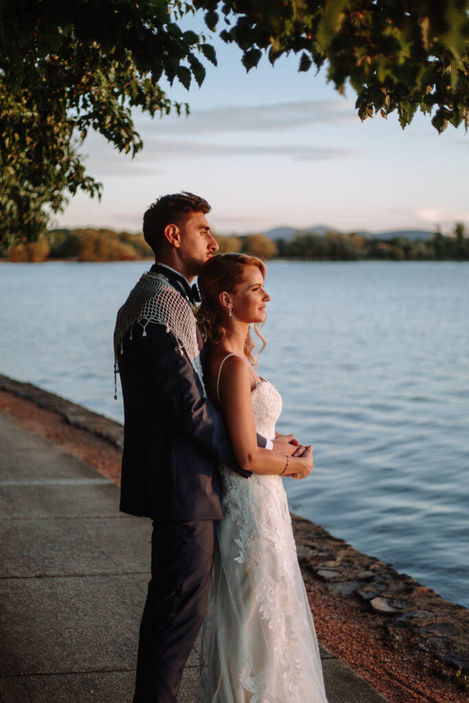 Becky and George embrace beneath a tree beside the water at The Boat House by the Lake.