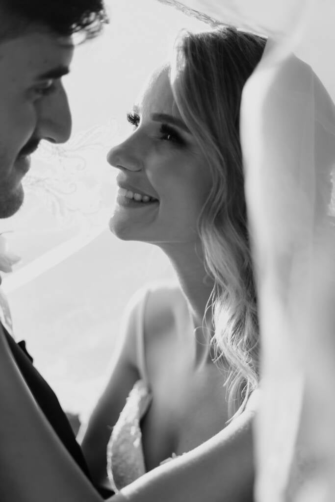 Black and white portrait of Becky and George smiling together beneath her veil.