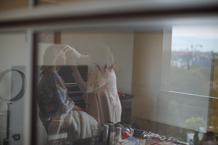 A makeup artist works on Sabine's face, seen through reflective glass