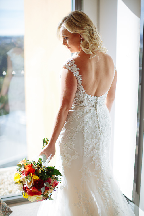 Sabine looks over her shoulder with her bouquet beside her low-backed lace gown