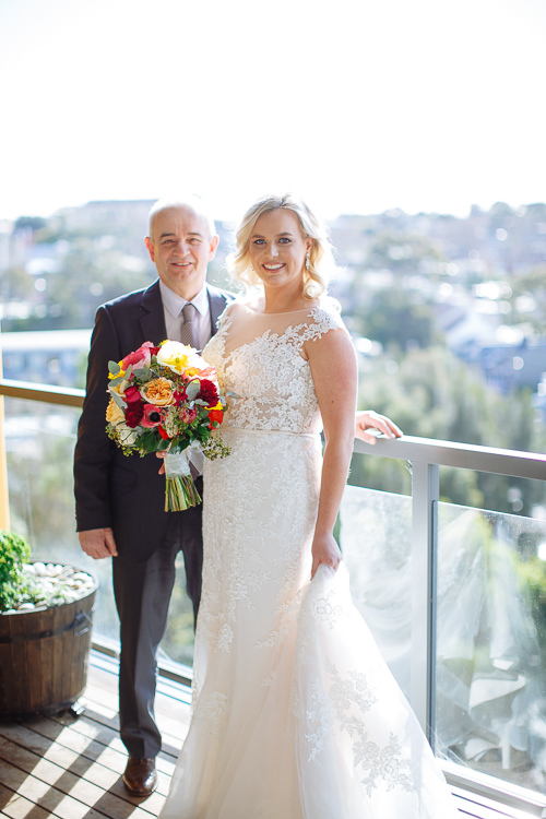 Sabine poses beside an older man on a balcony with her colourful bouquet