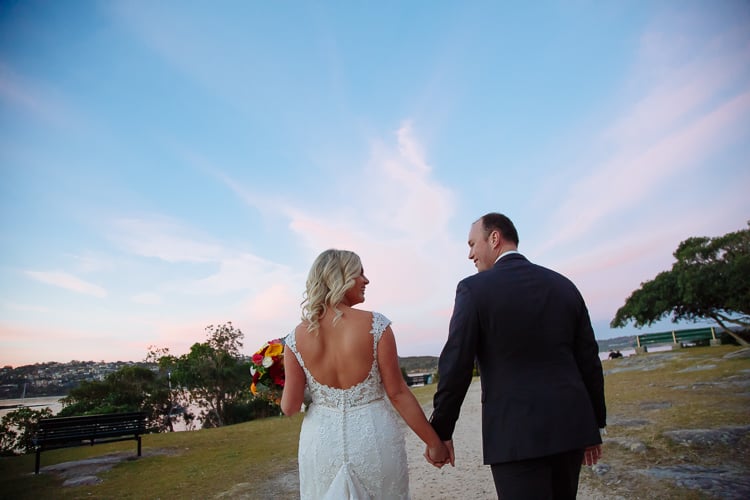 Sabine and Arthur walk hand in hand outside Bathers' Pavilion beneath a pink dusk sky
