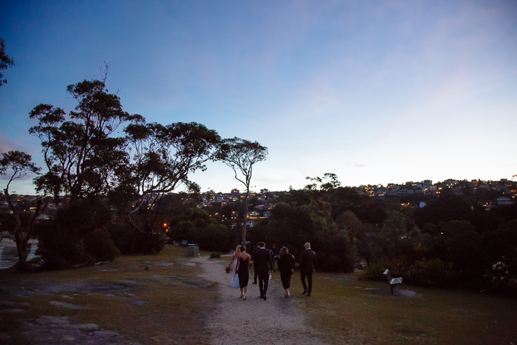 The wedding party walks along a tree-lined path near Bathers' at dusk