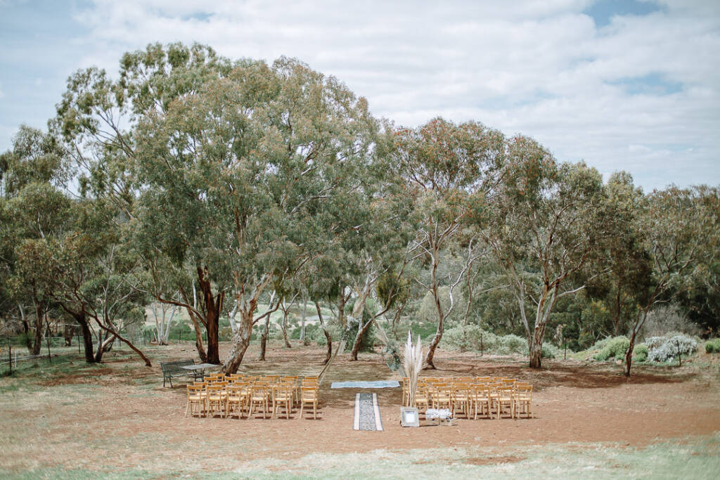 Timber chairs and a rug aisle frame the bush ceremony setting at Camp Sunnystones in Merrimu.