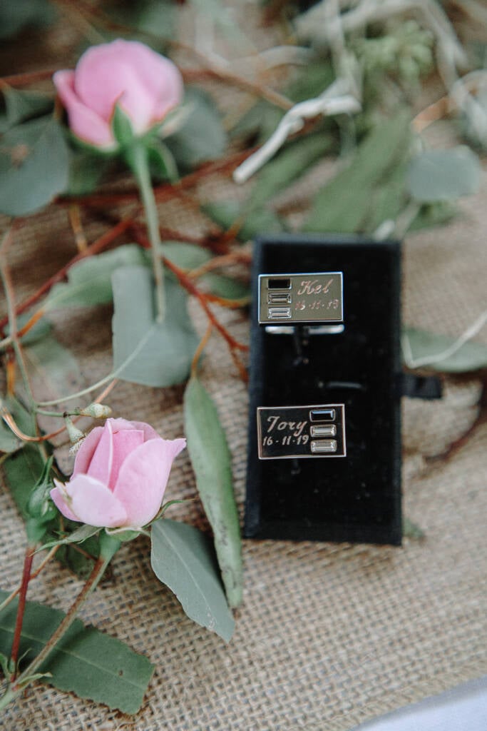 Engraved cufflinks lie among flowers and foliage before the wedding.