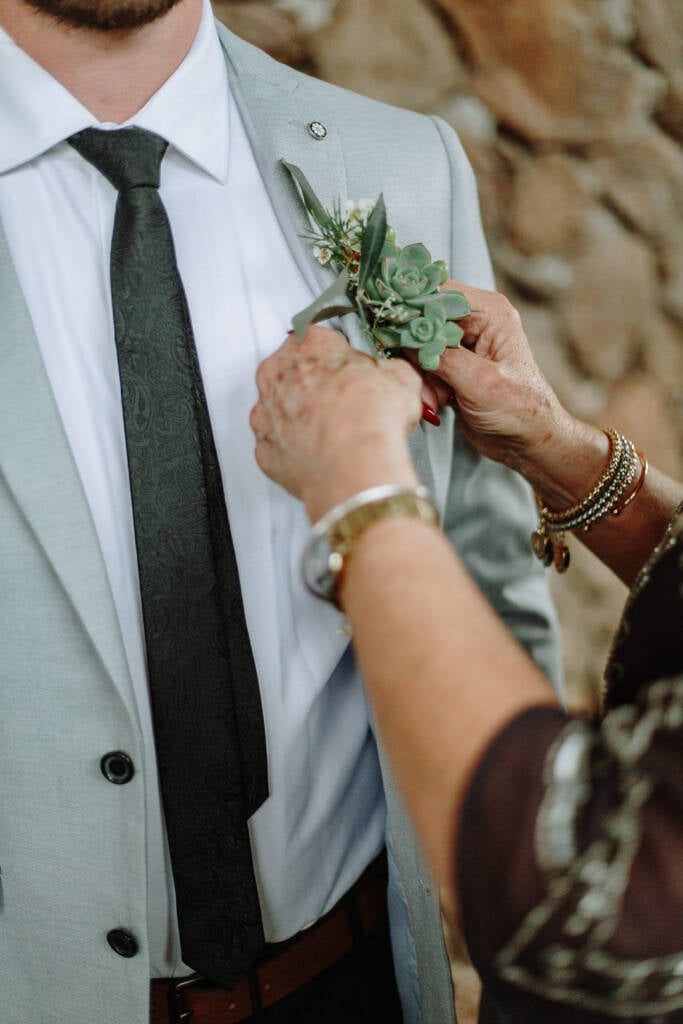 A succulent boutonniere is pinned to a pale-grey suit lapel.