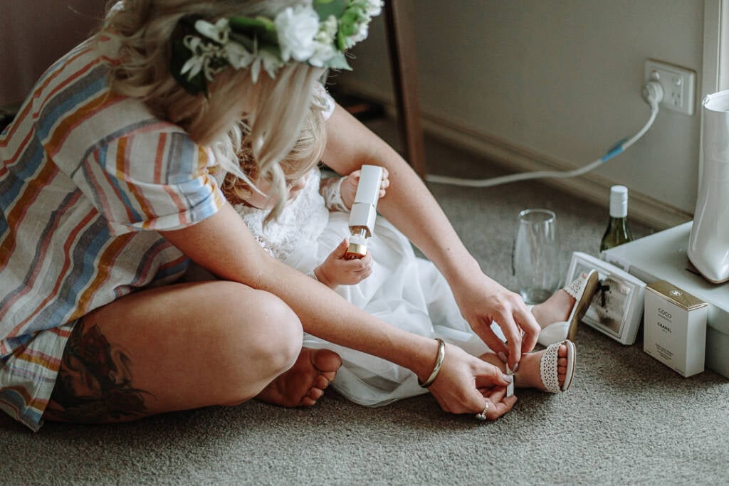 Kelly sits on the floor fastening a child’s sandal before the wedding.