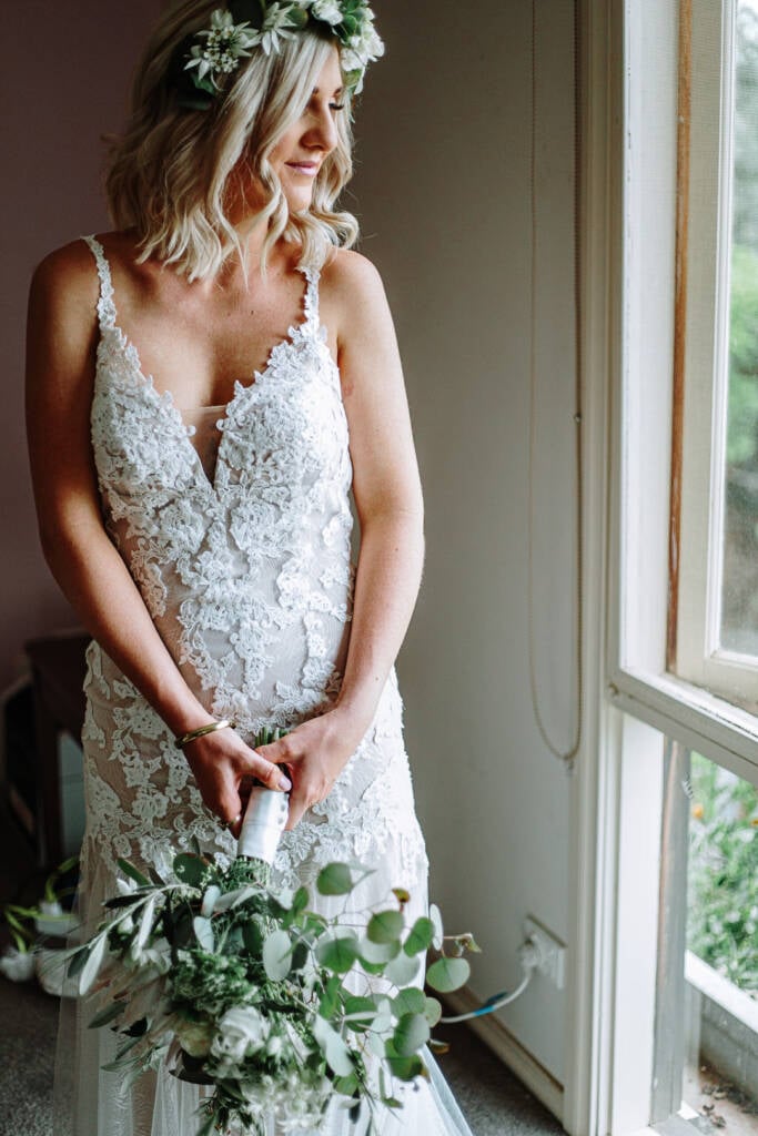 Kelly looks down in her lace wedding gown and flower crown at Camp Sunnystones.